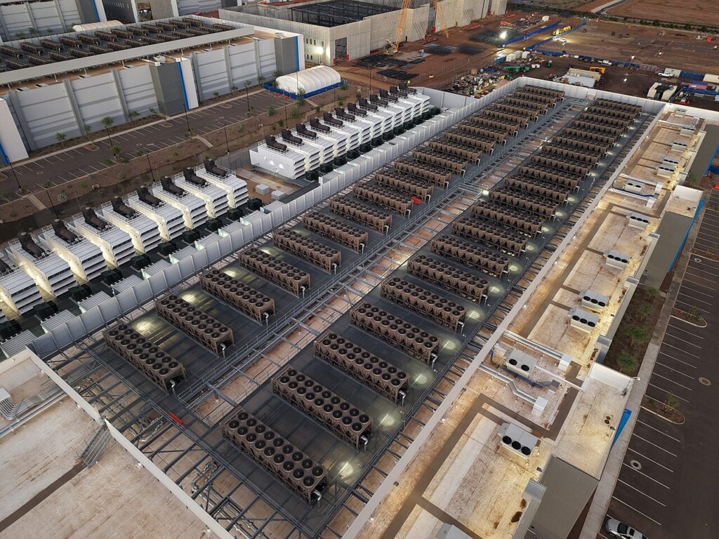 Aerial view of a large data-center roof with extensive rows of cooling equipment and supporting infrastructure.