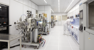 A cleanroom worker checks semiconductor process equipment in a fabrication bay, illustrating site-specific controls in a fab transfer.