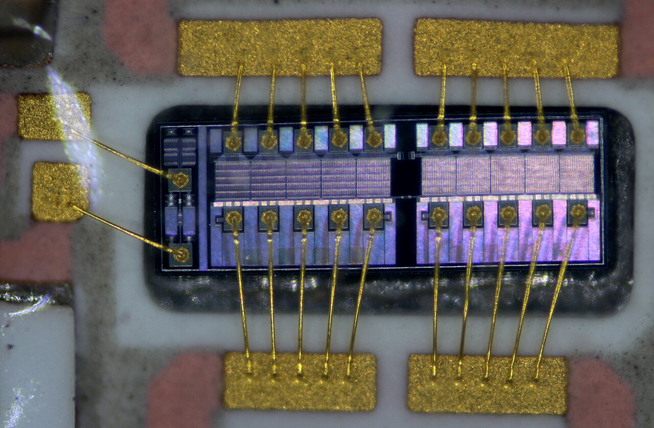 Close-up of one transistor die with visible structures and thin bond wires inside a hybrid amplifier